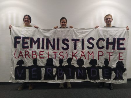 Das feministische Streikkomitee AUgsburg war zum Weltfrauentag bei uns im Studio zu Besuch - jetzt Inerview anhören. Moderatorin und Studiogäste halten Transparent